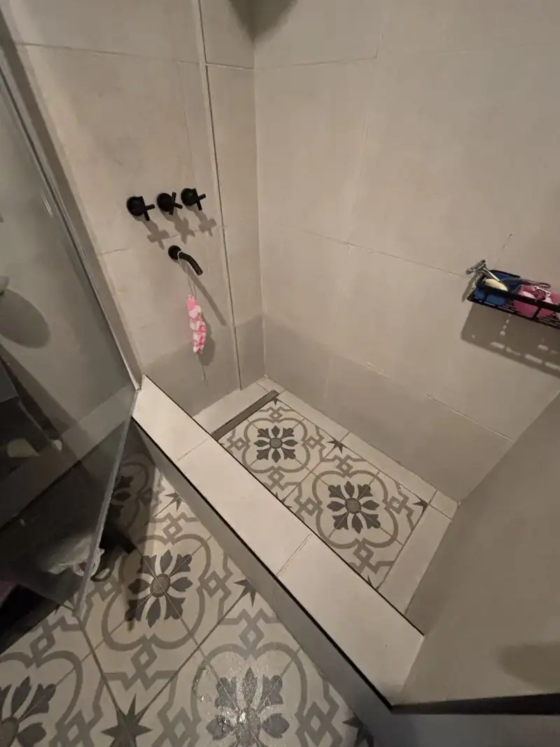 Ducha terminada con grifería negra, porcelanato de gran formato y piso de mosaico calcáreo