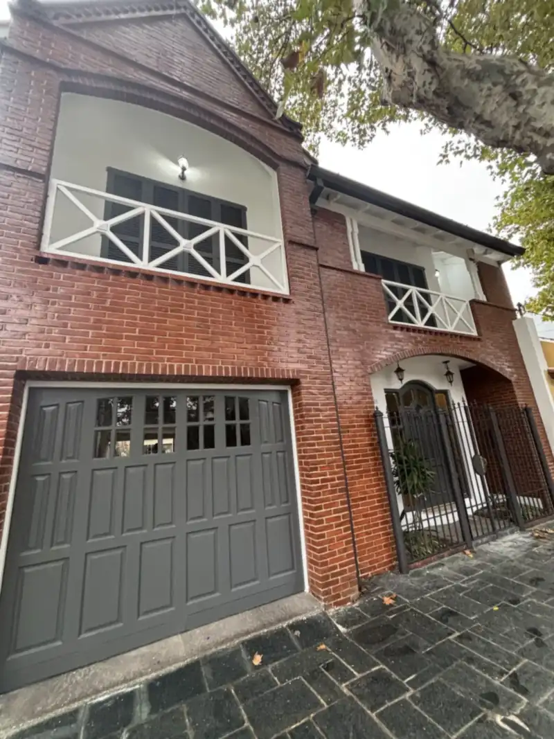 Frente de casa de ladrillo a la vista con balcón de baranda blanca y portón gris, recién pintado
